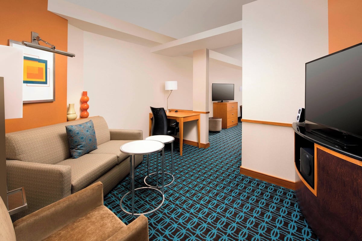 A hotel room with a sofa, a small table, a TV, and a desk with a chair.