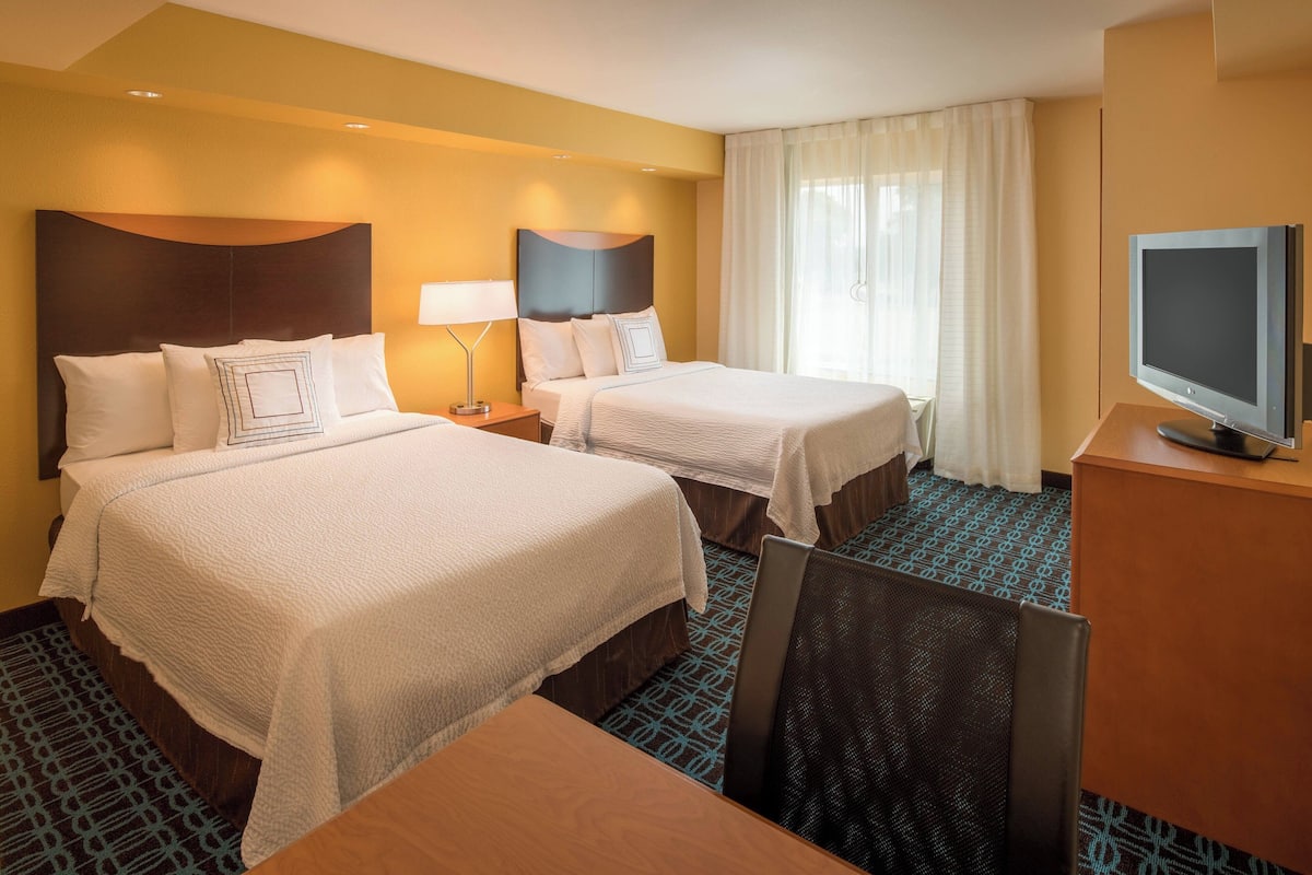 A hotel room with two beds, a desk, a chair, a television, and a window with curtains.