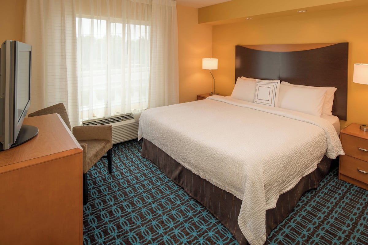 A hotel room with a large bed, a desk with a television, a chair, and a window with curtains.