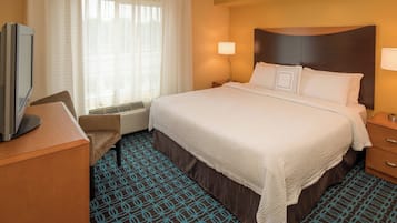A hotel room with a large bed, a desk with a television, a chair, and a window with curtains.