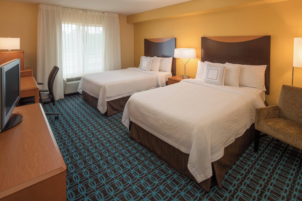 A hotel room with two beds, a desk with a television, a chair, and a patterned carpet.