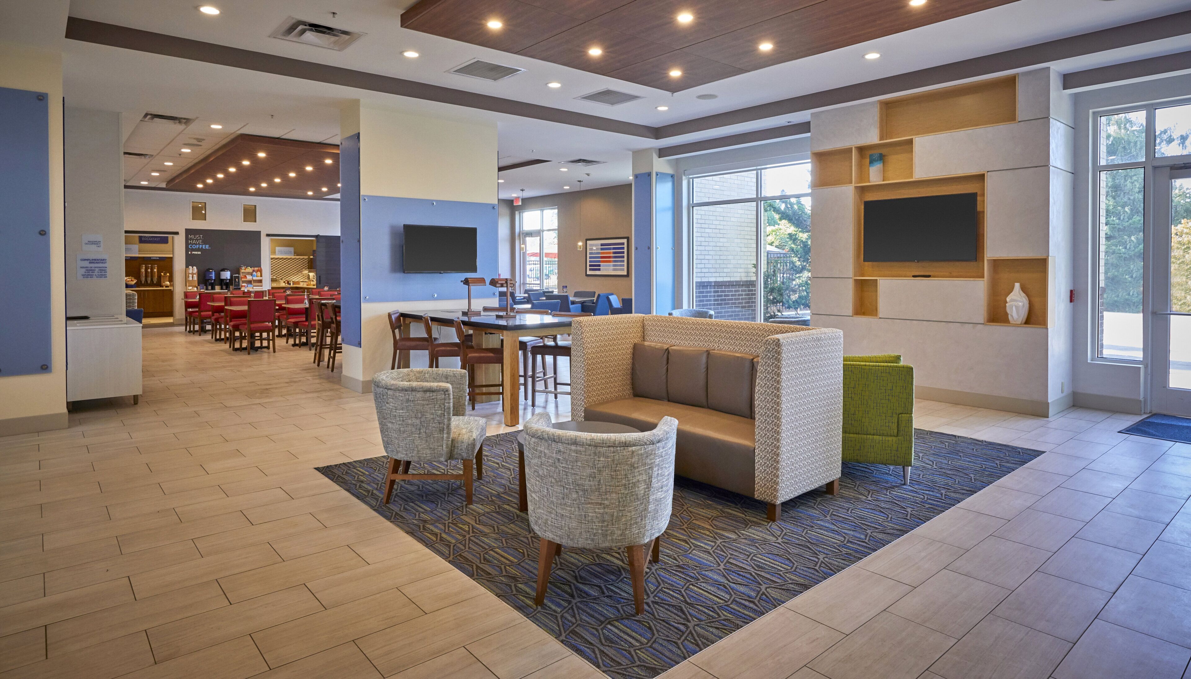 A hotel lobby with a seating area, a coffee station, and a large window providing a view of the outdoors.