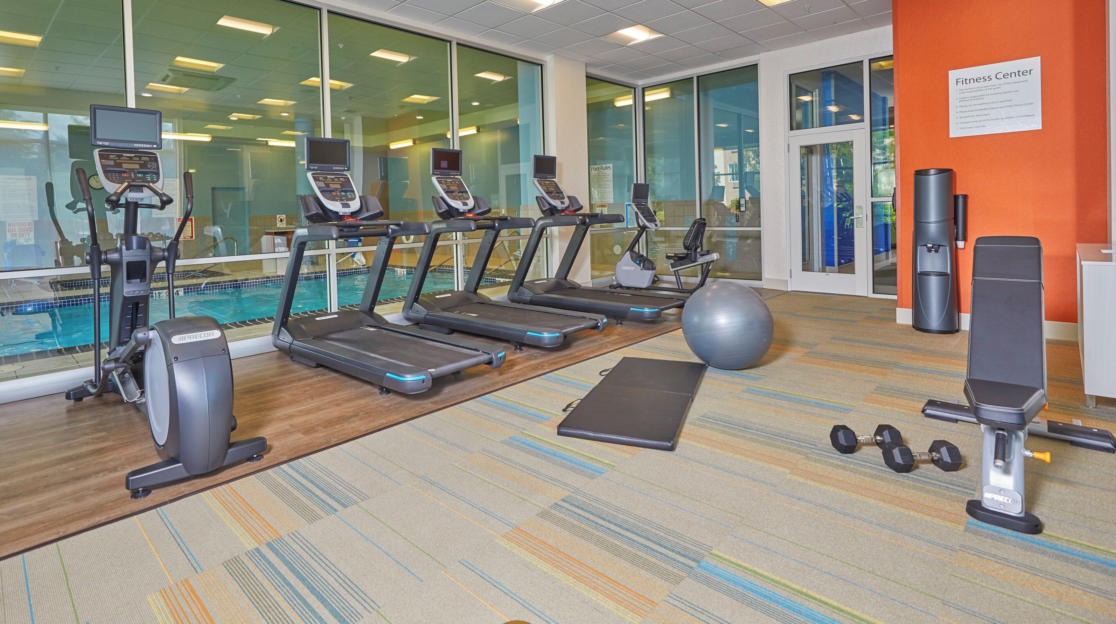A fitness center with treadmills, an exercise ball, dumbbells, and a pool in the background.