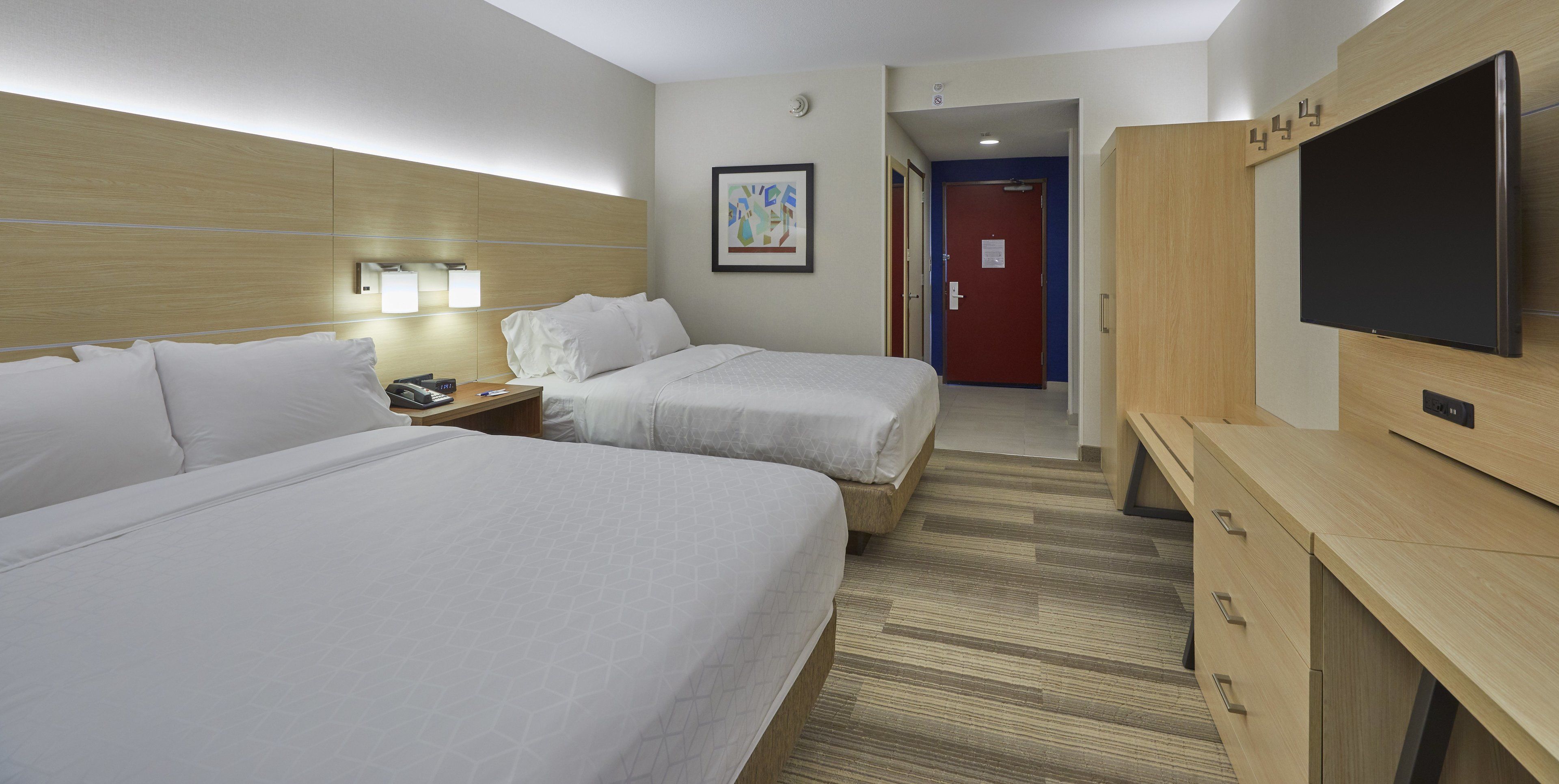 A hotel room with two beds, a desk, a TV, and a door leading to another room.
