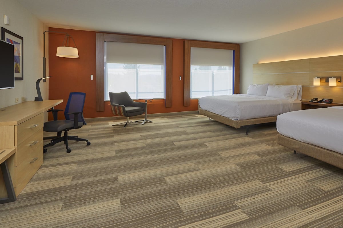 Habitación de hotel con dos camas, un escritorio, una silla y un televisor.