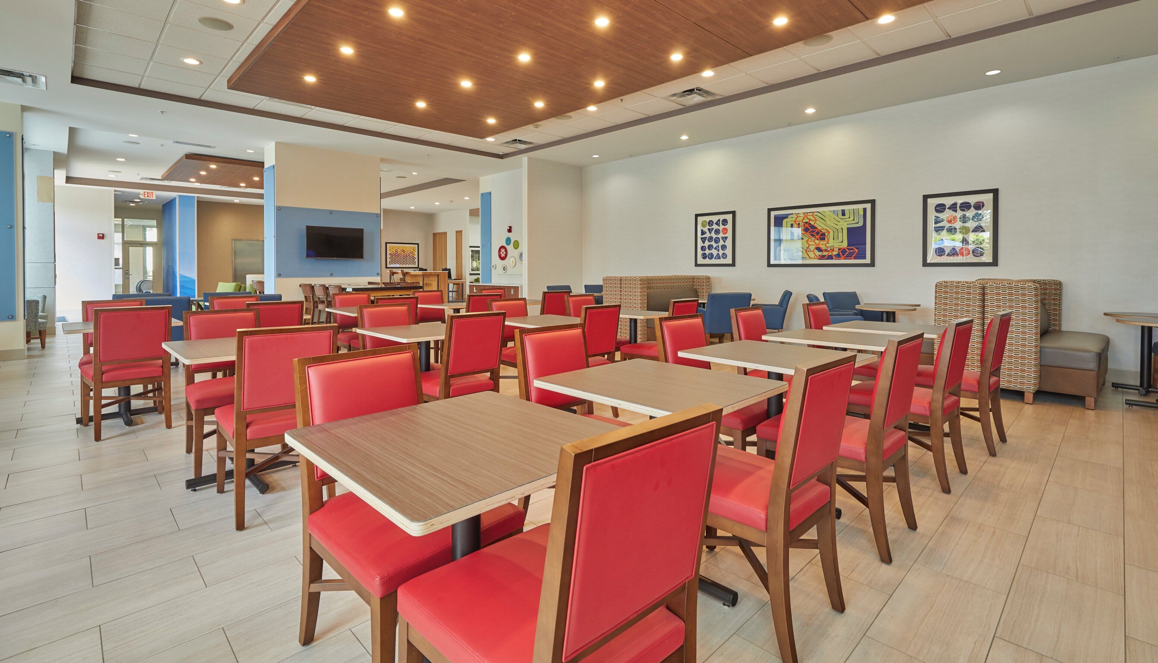 A modern dining area with multiple tables and chairs, a flat-screen TV mounted on the wall, and artwork on the walls.