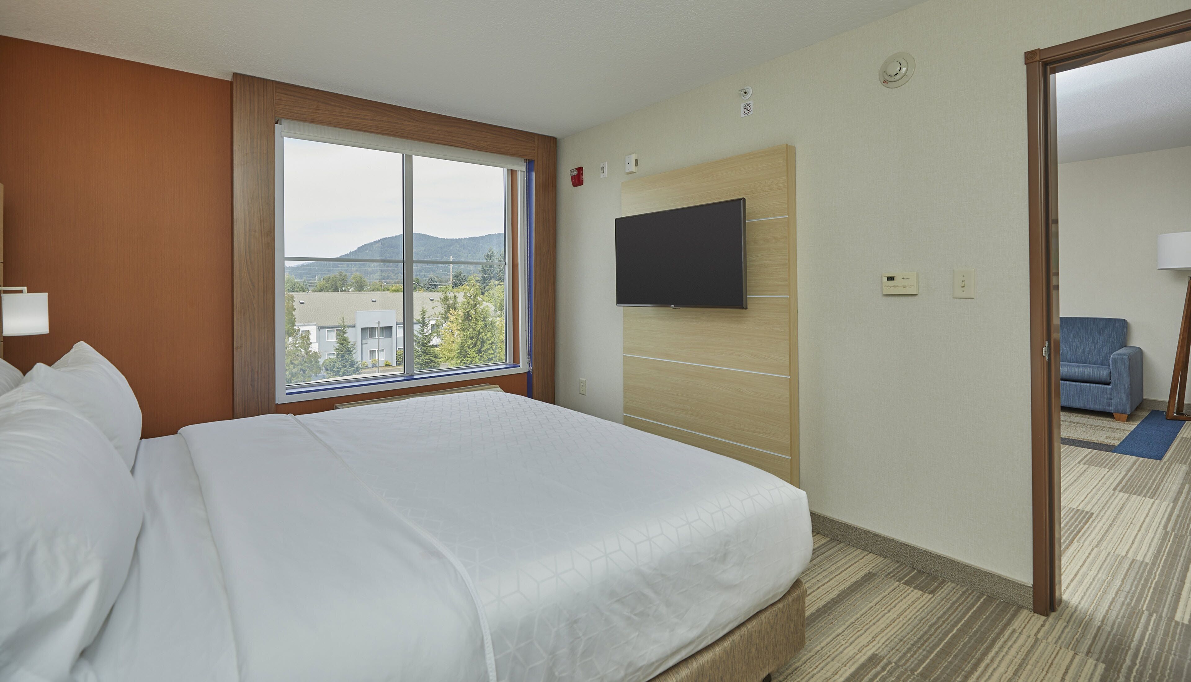 Una camera d'albergo con un letto grande, una televisione a muro e vista all'esterno tramite una finestra.