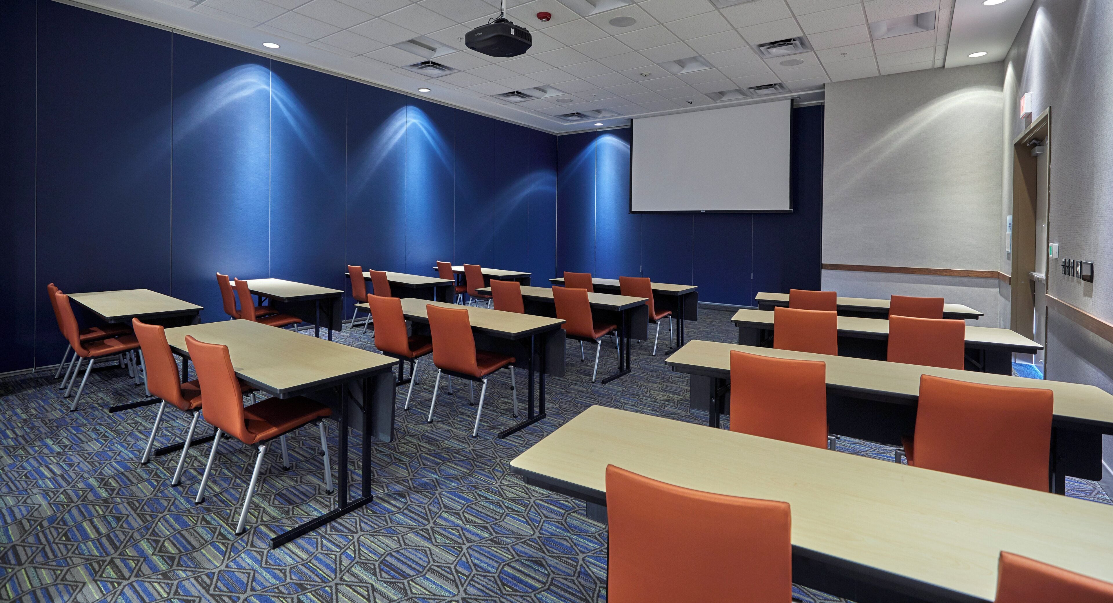 A conference room with tables and chairs, a projector screen, and a presentation screen.