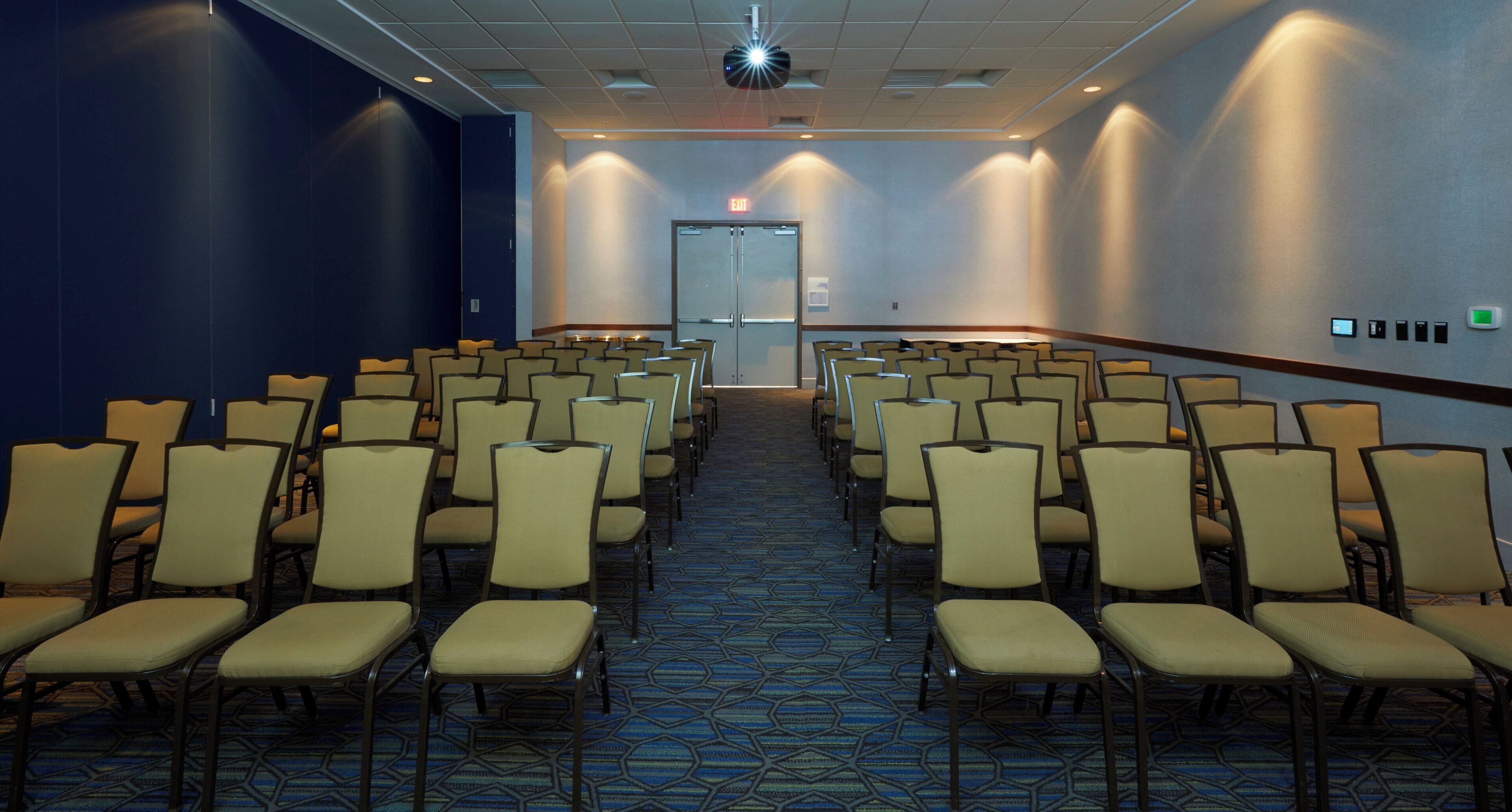 A conference room with rows of chairs, a carpeted floor, and a door at the end.