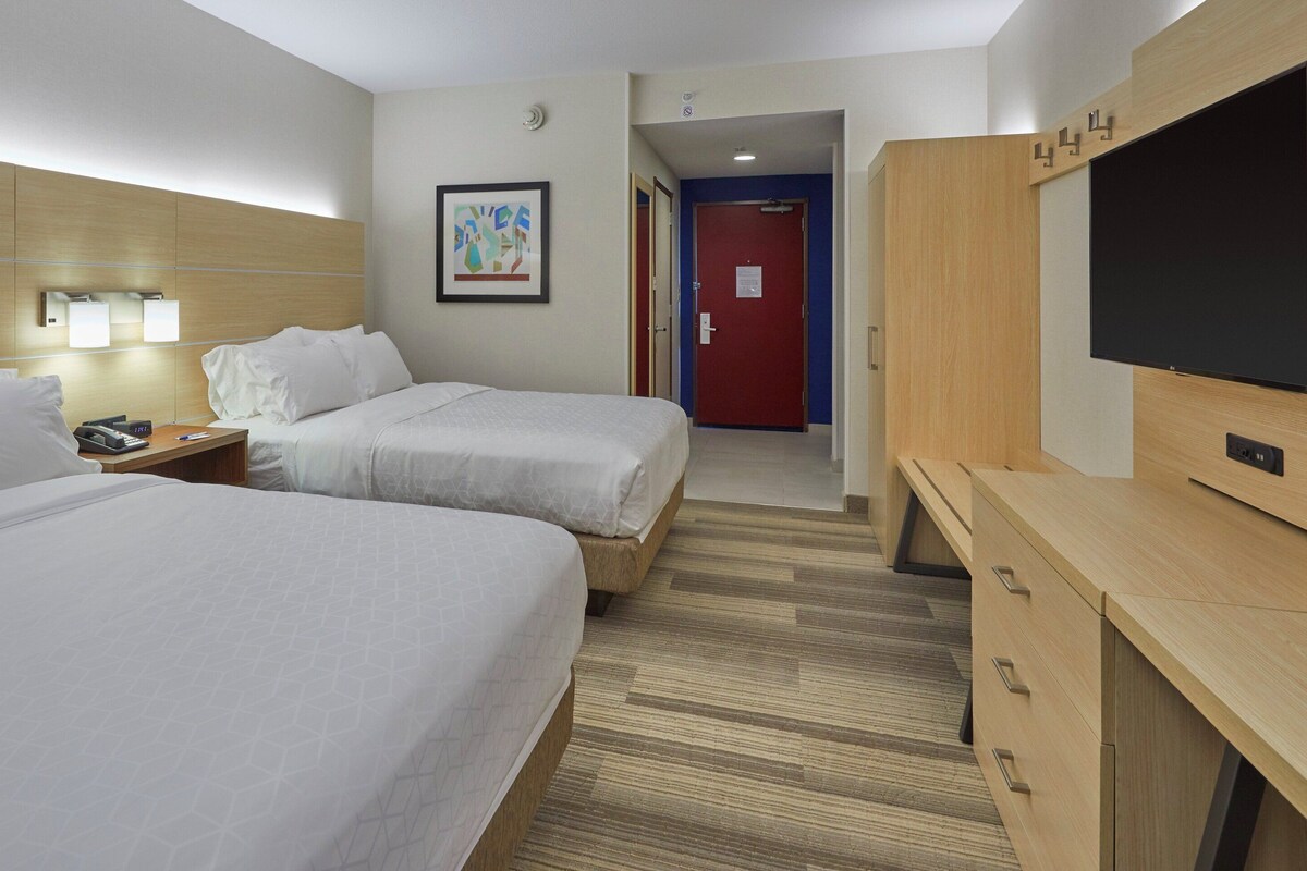 A hotel room with two beds, a desk with a telephone, a television, and a door leading to another room.
