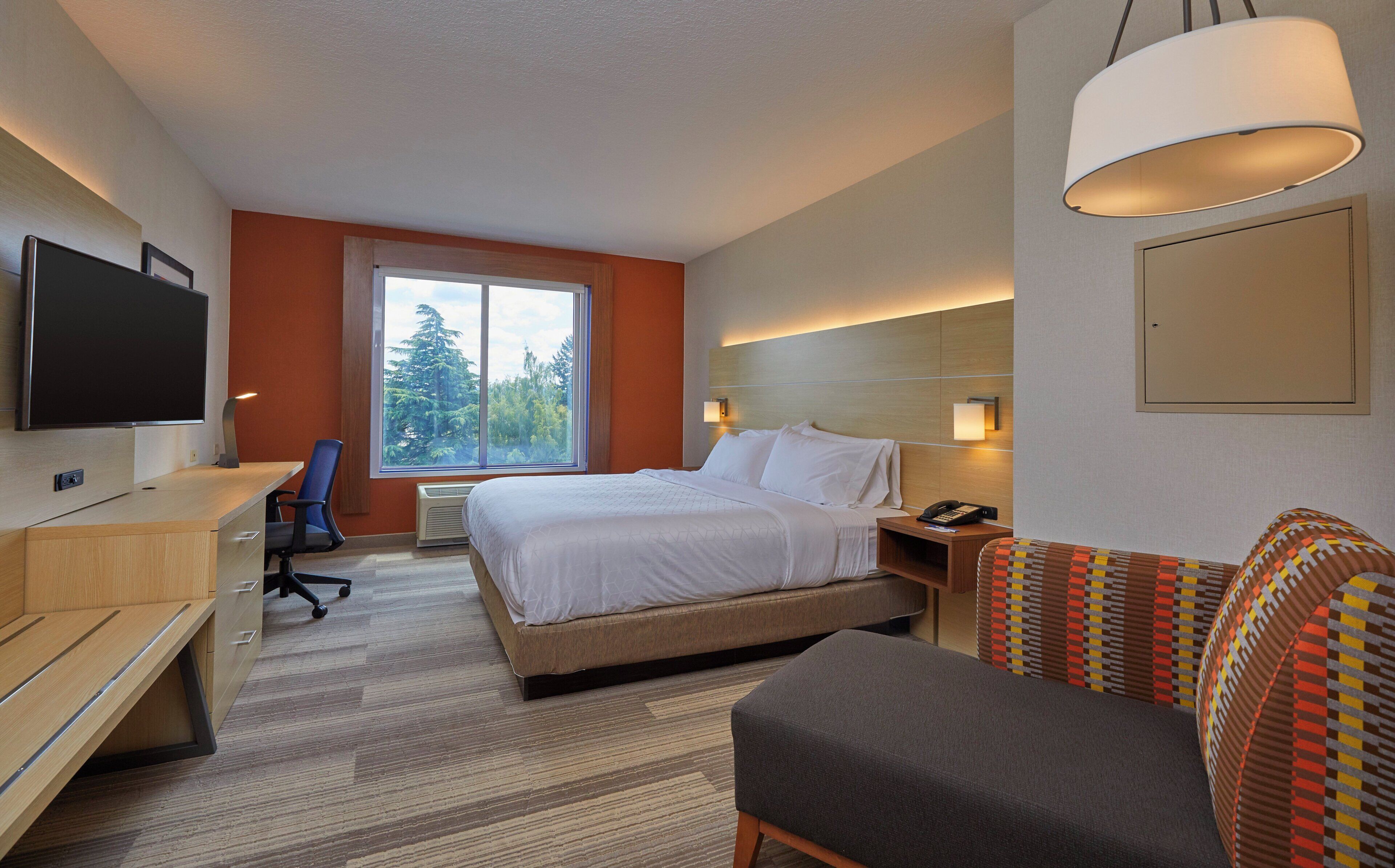 A hotel room with a bed, desk, chair, and a television.