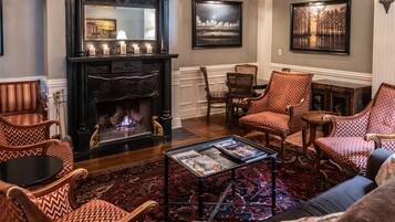 Una sala de estar acogedora con chimenea, sillas estampadas, una mesa de centro con revistas y una alfombra grande.