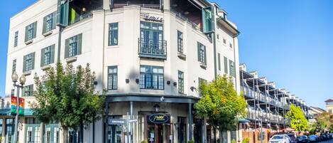 Un edificio en esquina con un restaurante en la planta baja, varios balcones y una fila de coches aparcados a lo largo de la calle.