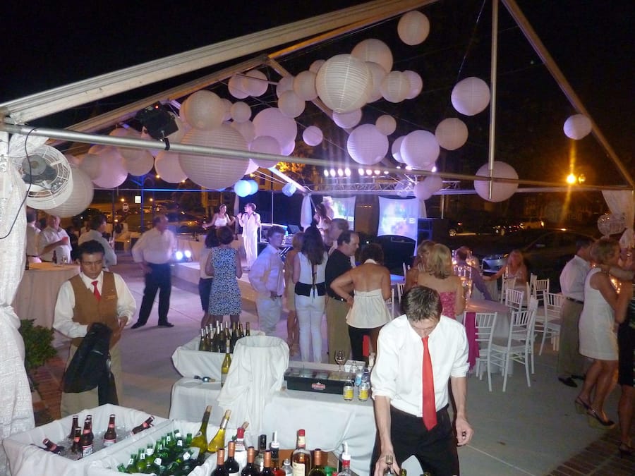 An outdoor event with a tent, tables with bottles, and people mingling.