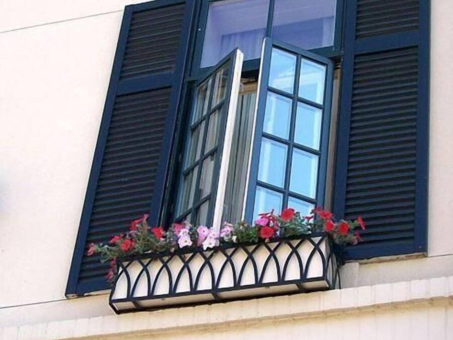 Un bâtiment doté d’une fenêtre ornée de volets noirs et d’une jardinière contenant des fleurs roses et rouges.