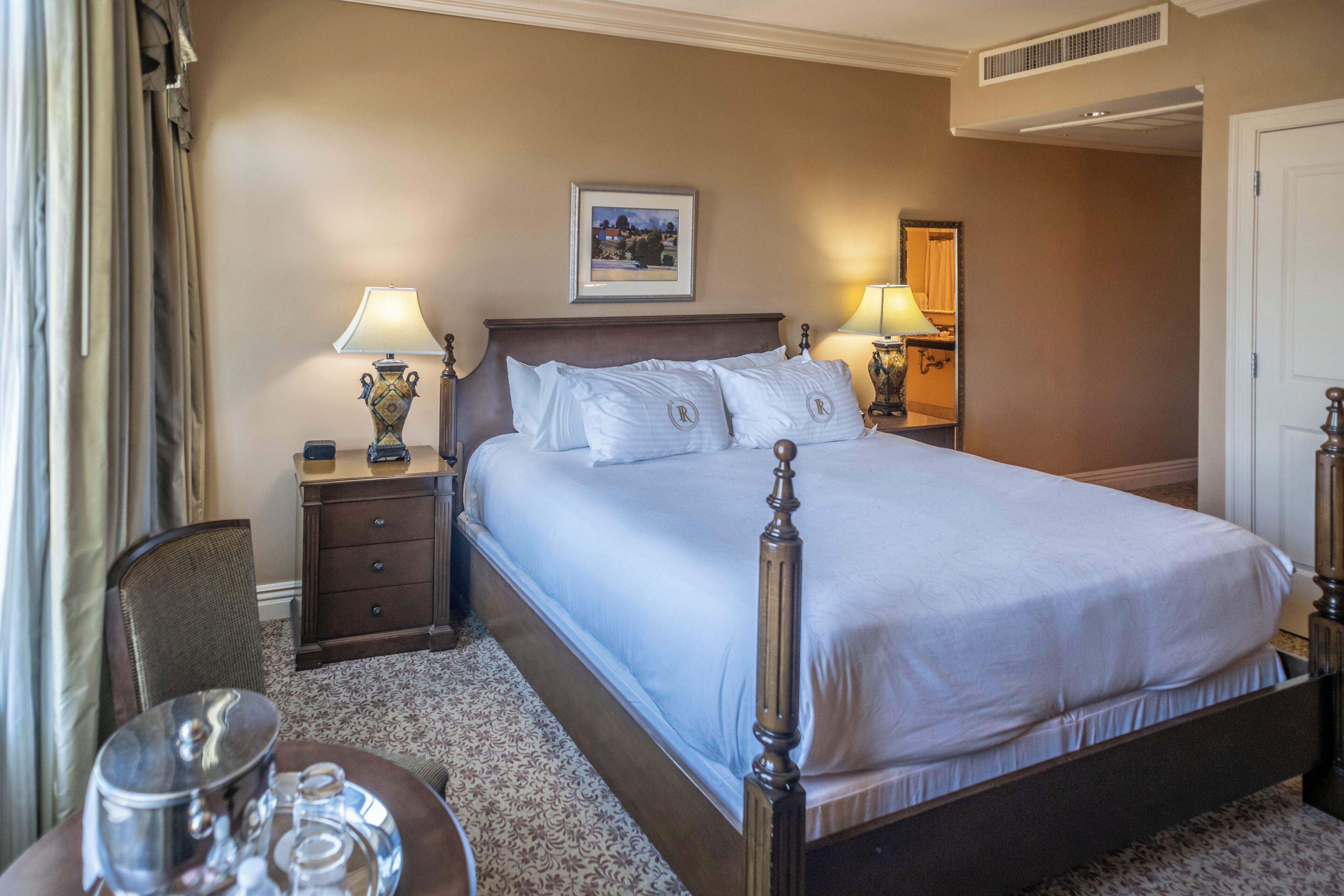 A neatly arranged hotel room with a large bed, two bedside tables with lamps, a chair, and a small table with a tray.