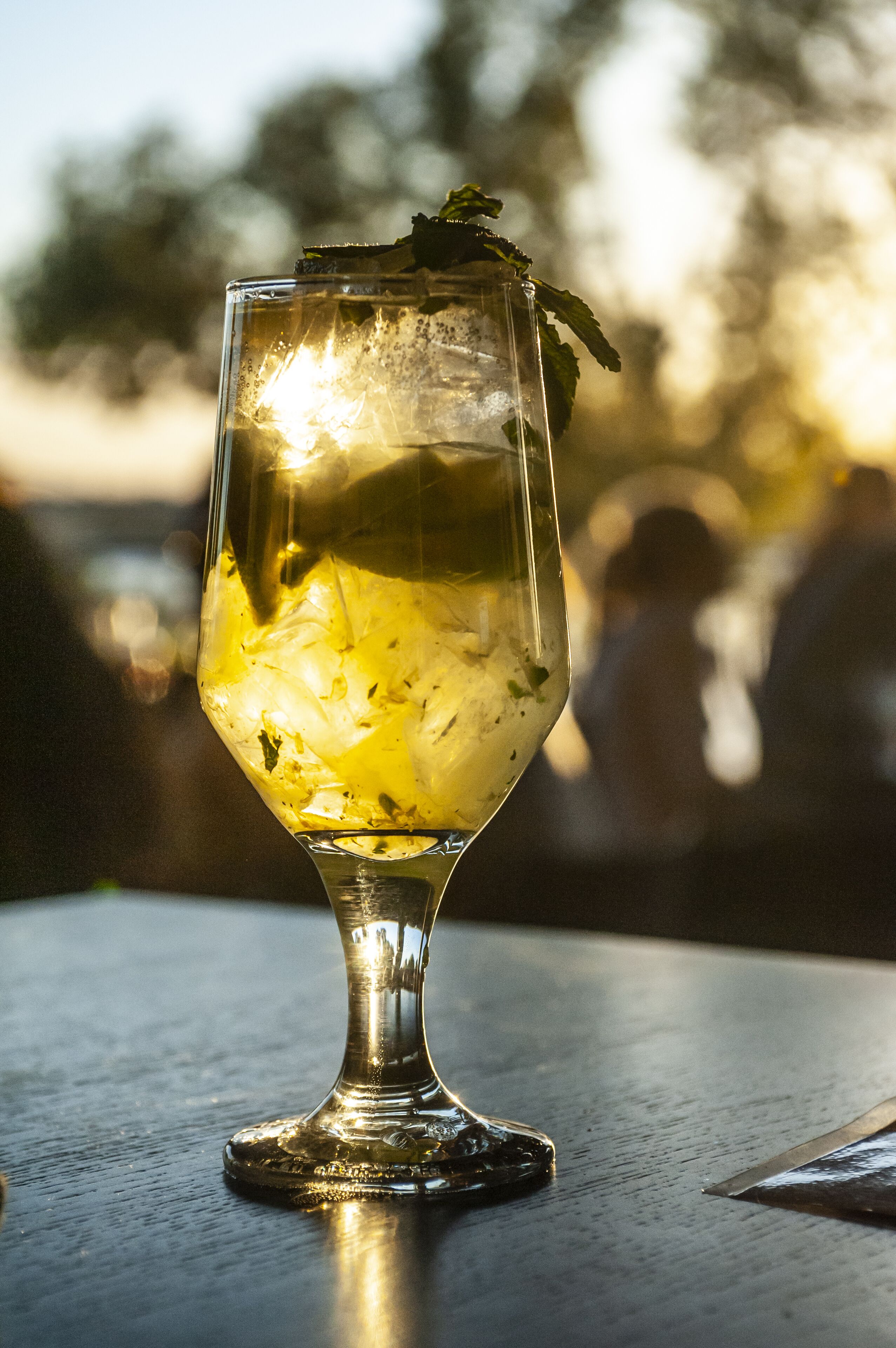 A glass of a beverage with mint leaves on a table outdoors.