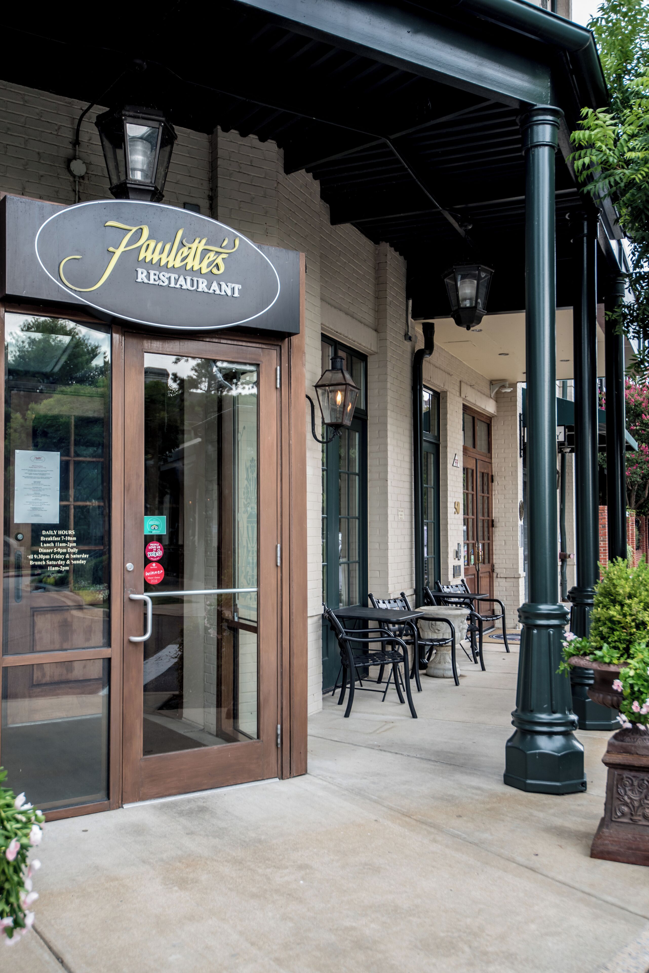 A restaurant entrance with a sign, outdoor seating, and a covered patio area.