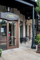 A restaurant entrance with a sign, outdoor seating, and a covered patio area.