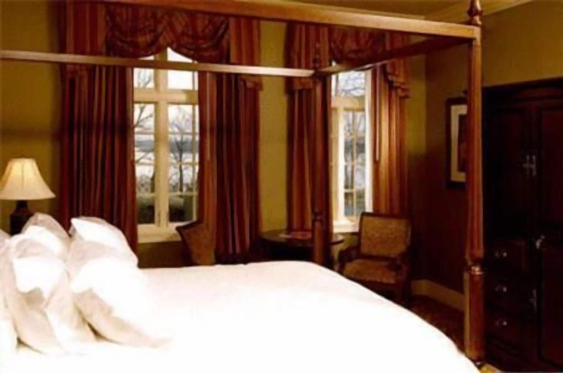 A hotel room with a large bed, a chair, a desk, and a wardrobe.