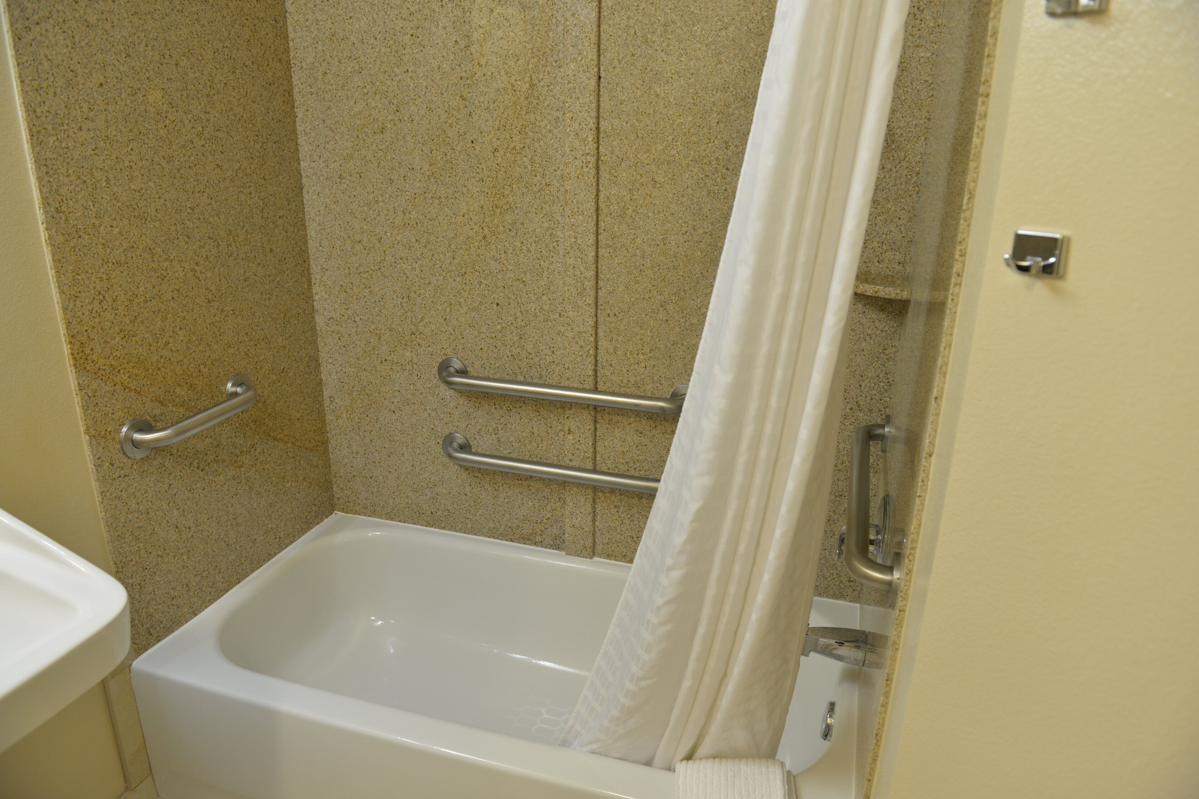 A standard bathroom with a bathtub, grab bars, and a shower curtain.