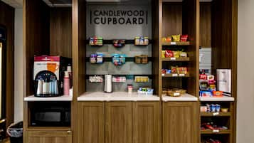A kitchenette with a coffee machine, microwave, and shelves stocked with snacks and beverages.