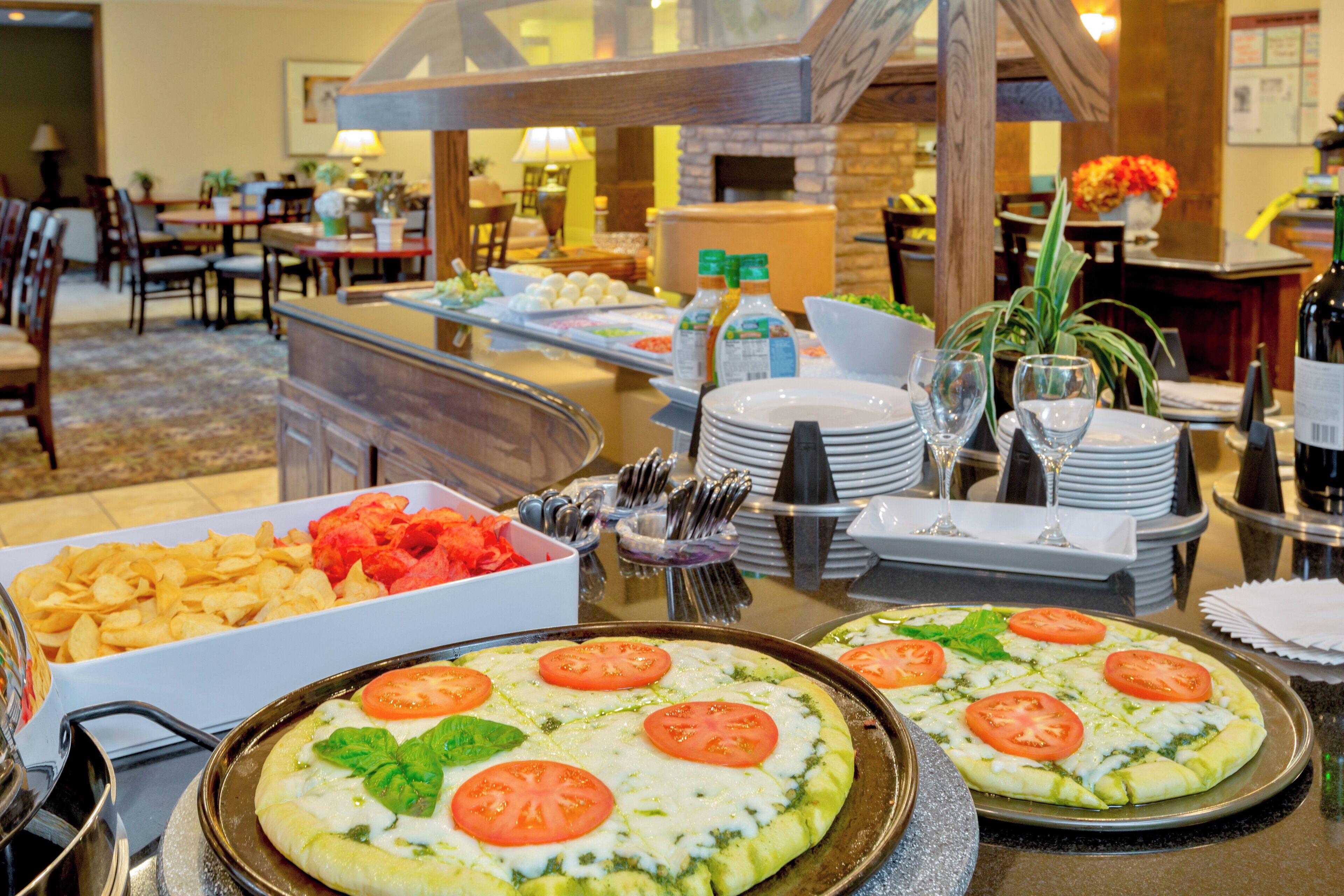 A buffet setup with various food items and a pizza with tomatoes and basil.