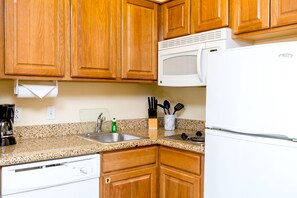 A kitchen with wooden cabinets, a white microwave, a sink, and a dishwasher. - Staybridge Suites McAllen by IHG (McAllen)