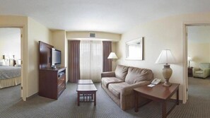 A hotel room with a bed, a TV, a sofa, a small table, a lamp, and a chair. - Staybridge Suites McAllen by IHG (McAllen)