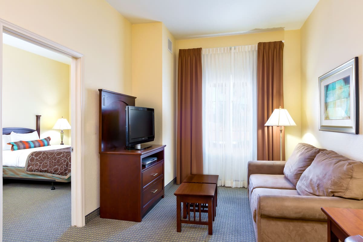 A hotel room with a bed, a television on a wooden stand, a sofa, a small table, and a lamp.