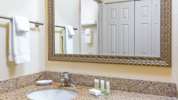 Casa de banho com bancada de granito, lavatório branco, espelho com moldura decorativa e toalheiro com toalhas brancas.