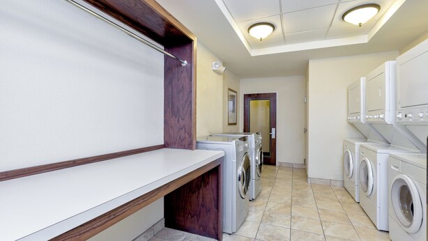 A laundry facility with multiple washing machines and dryers, a wooden bench, and a tiled floor. - Staybridge Suites McAllen by IHG (McAllen)