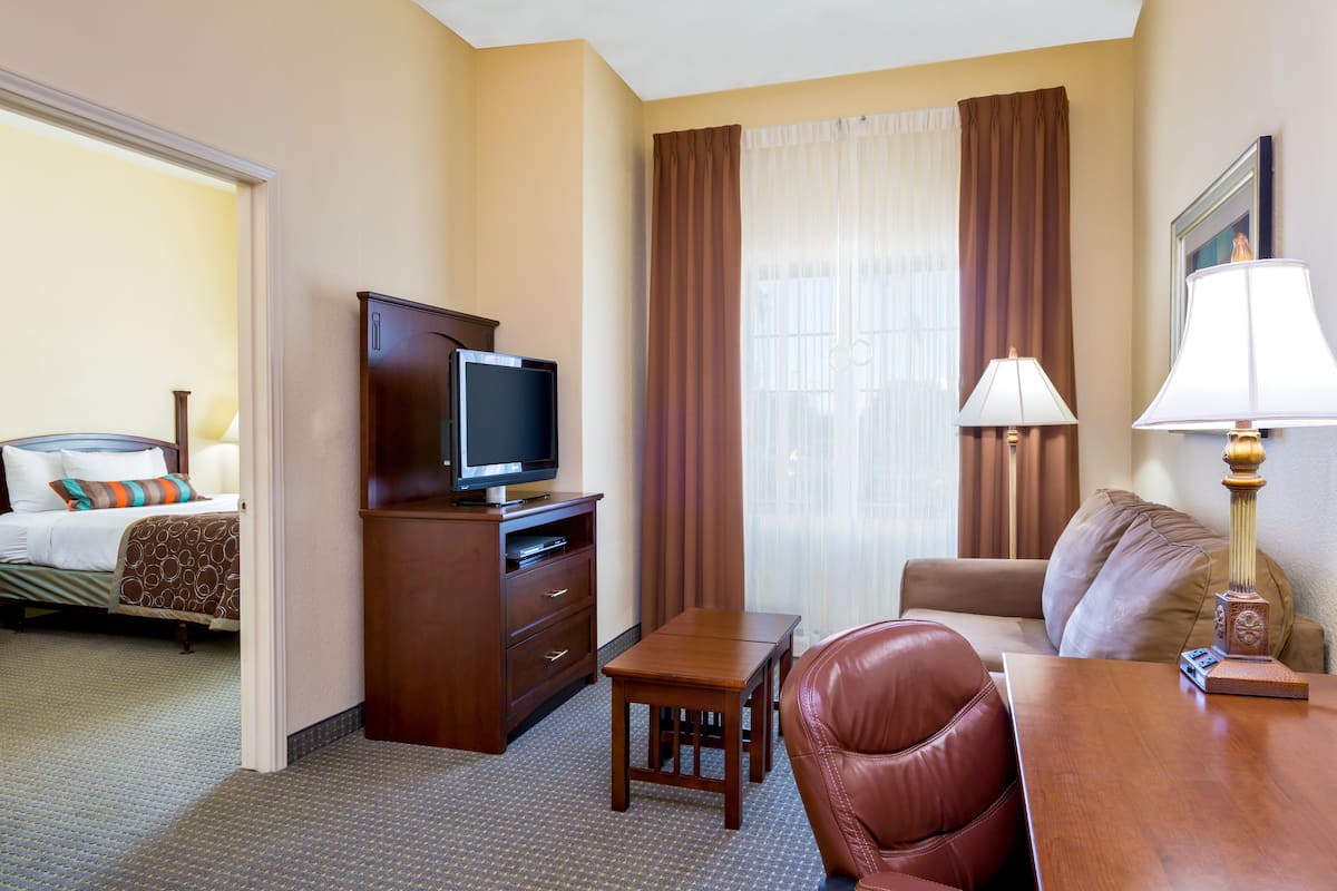 A hotel room with a bed, a television on a wooden cabinet, a desk with a lamp, a leather chair, and a sofa.