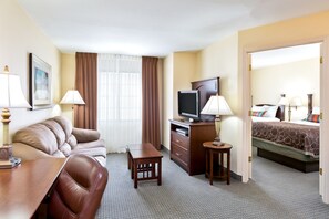 A hotel room with a brown leather sofa, a wooden desk, a television, a small table, and a bed with a patterned bedspread. - Staybridge Suites McAllen by IHG (McAllen)