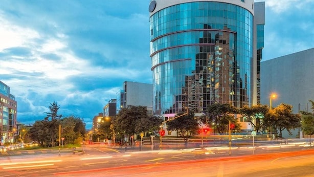 Un edificio moderno con fachada de vidrio curva, rodeado de árboles y farolas.