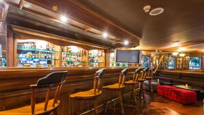 Un área de bar con taburetes de madera, una pantalla de televisión y estantes con botellas.