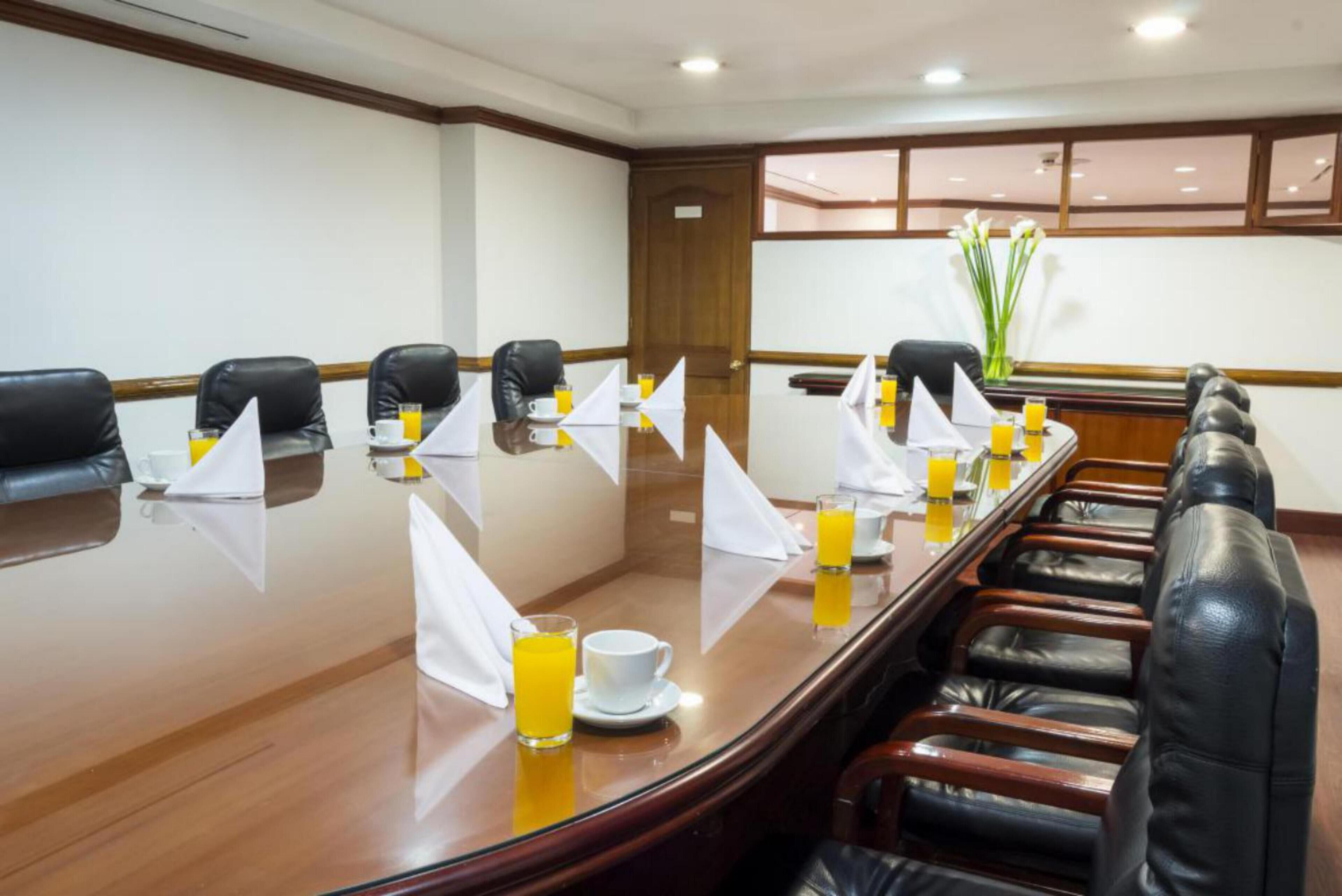 A conference room with a long table, black leather chairs, and white napkins.