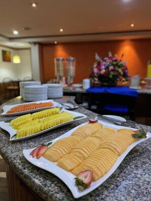 A buffet setup with various food items including sliced fruits and pastries on a granite countertop. - Hotel Bogotá Regency Usaquén (Bogotá)