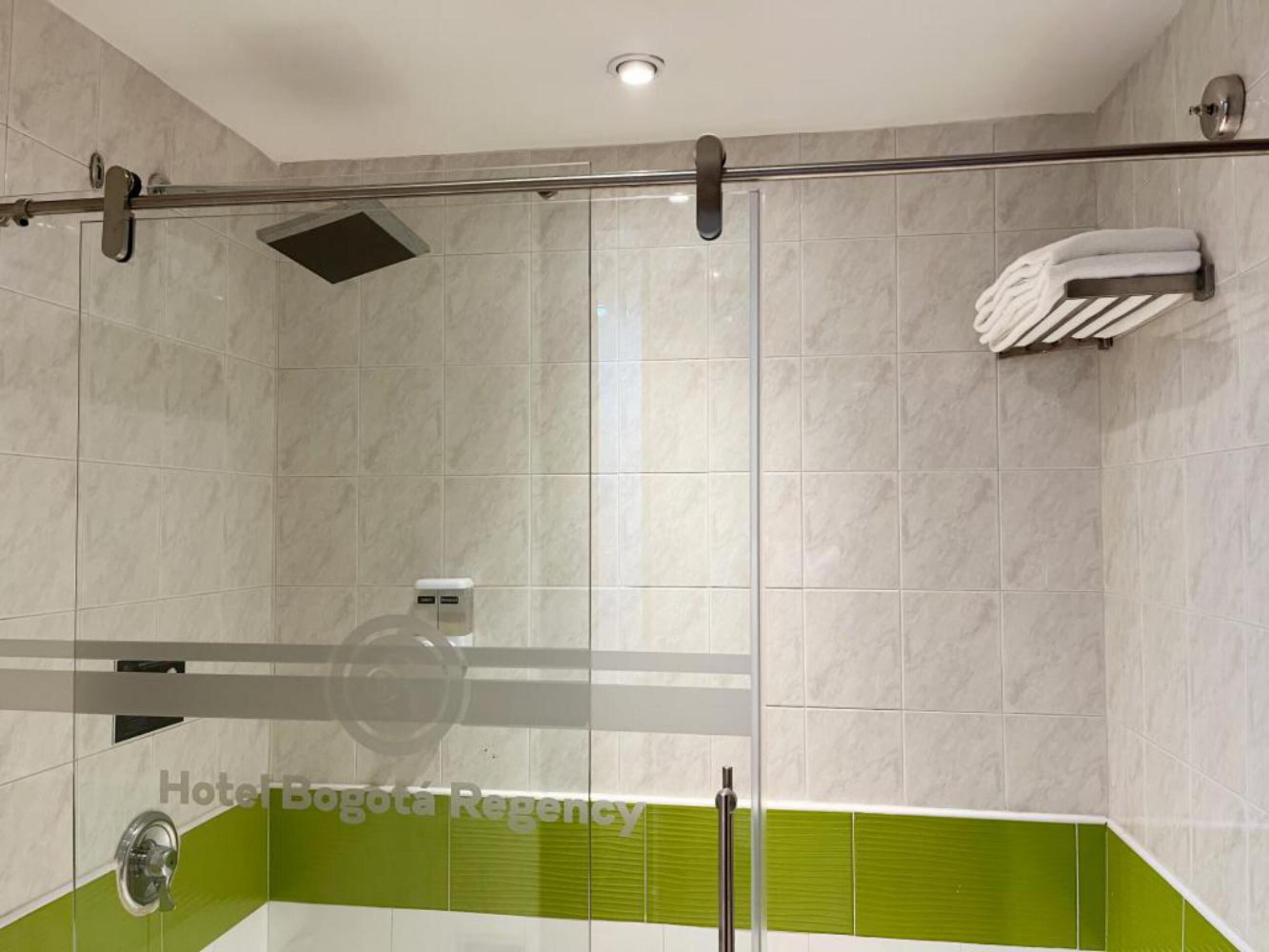 A modern bathroom with a glass shower enclosure, a towel rack, and a green accent wall.