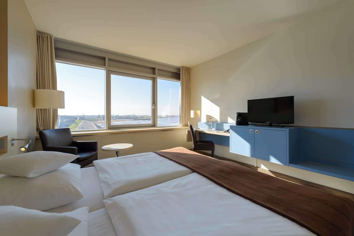 Een hotelkamer met twee bedden, een bureau, een televisie en uitzicht op de stad.