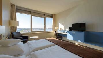 Habitación de hotel con dos camas, un escritorio, televisión y vistas a la ciudad.
