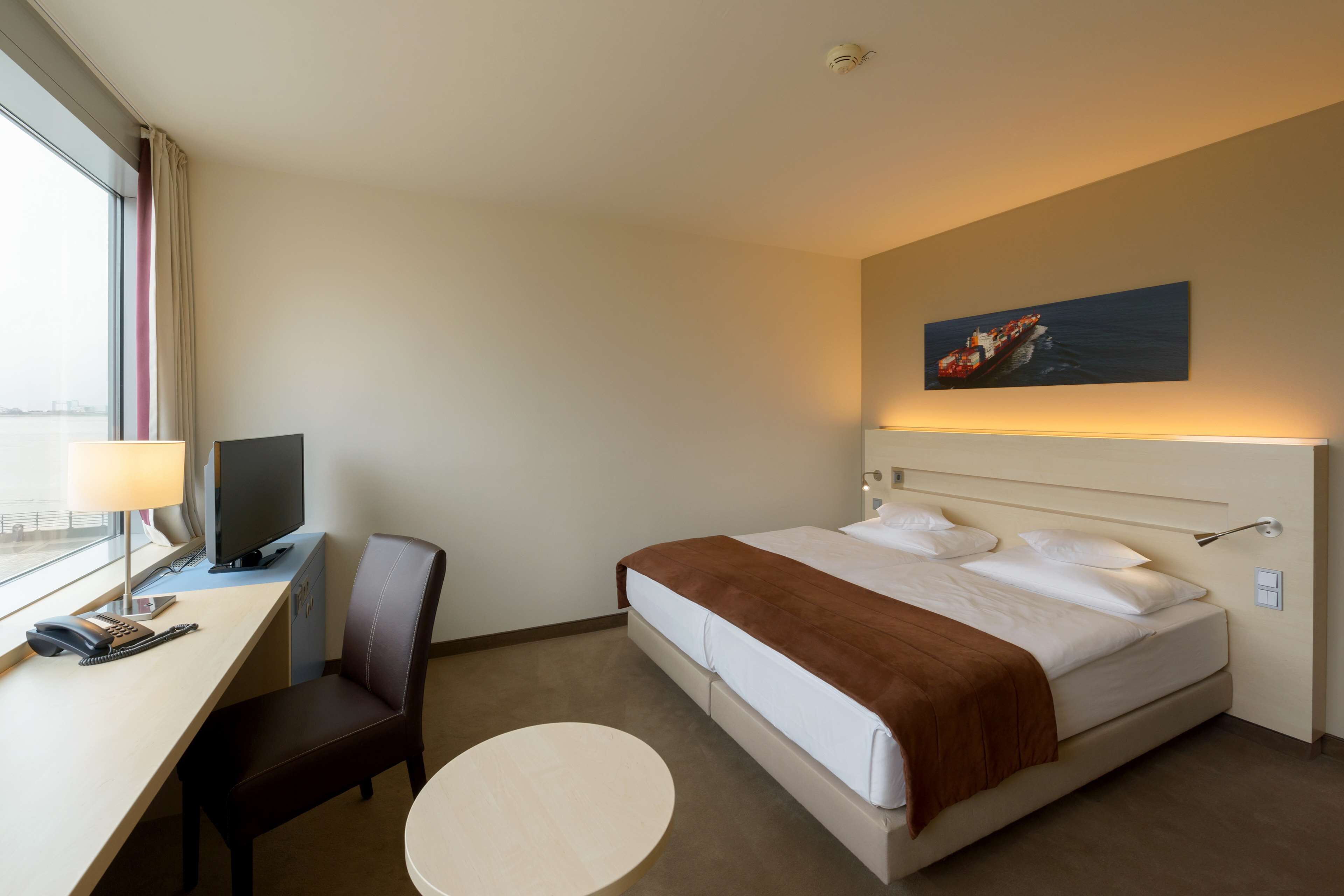 A hotel room with a bed, desk, chair, and a round table.