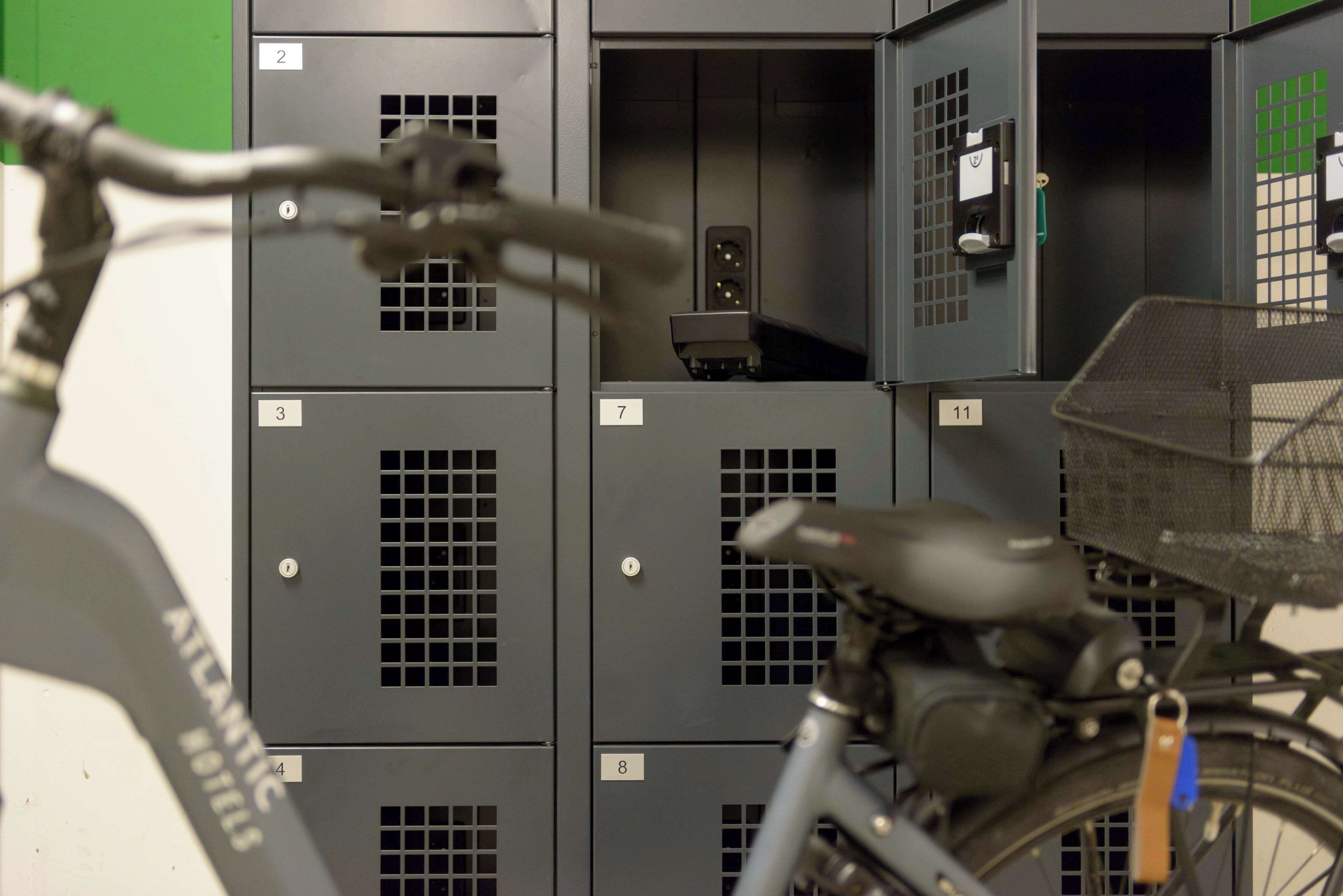 A bicycle with a basket, parked in front of a row of numbered lockers.