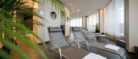 A spa room with reclining chairs, large windows, and potted plants.
