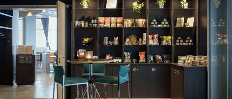 A restaurant interior with a bar area, green upholstered bar stools, and shelves stocked with various food items and condiments.