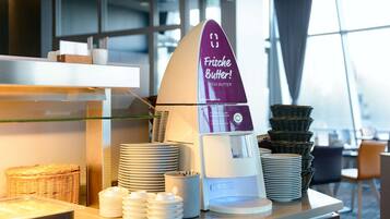 Un buffet avec un présentoir à beurre où les clients peuvent se servir eux-mêmes, ainsi que des assiettes et des paniers.