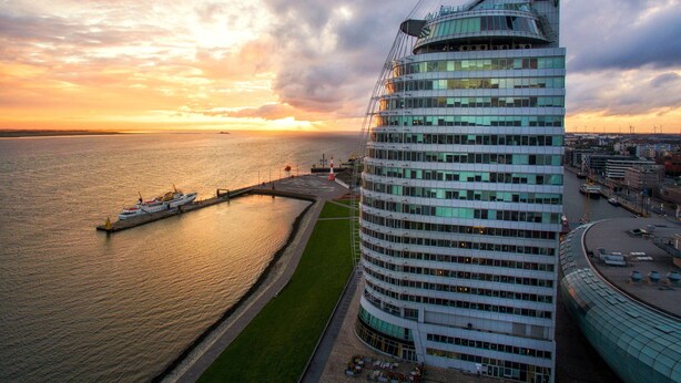 A modern building with a curved facade, a waterfront view, and a dock with a boat.
