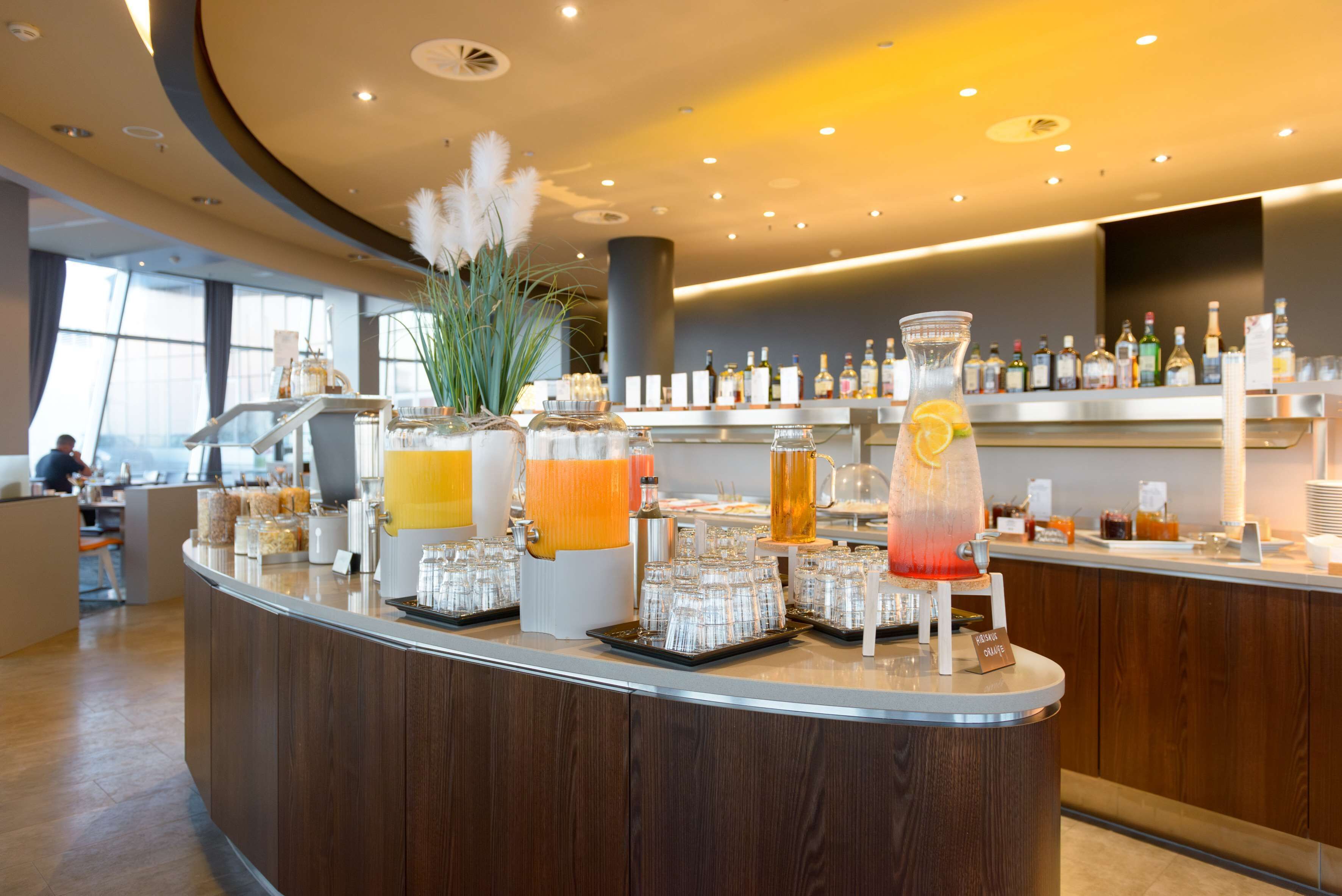 Eine moderne Bar mit einer Auswahl an Getränken, einer großen Vase mit weißen Blumen und einer gut beleuchteten Innenraumgestaltung.