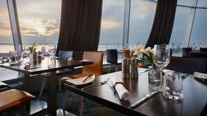 A dining area with tables set for two, featuring a view of the ocean through large windows.