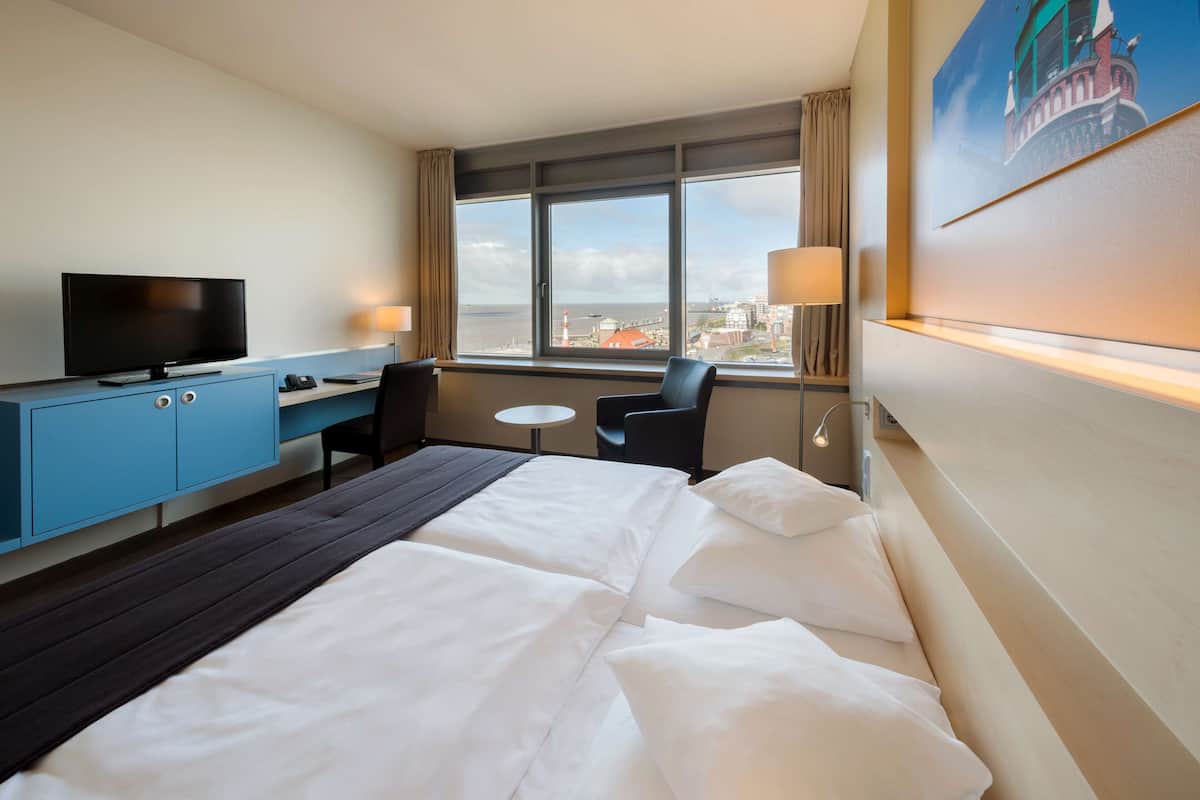 Een hotelkamer met een bed, een bureau met een televisie, een stoel, een klein tafeltje en een raam met uitzicht op de stad.